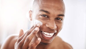 Portrait of a handsome young man applying moisturizer to his face in the bathroom at home