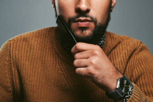 Cropped studio shot of a young man combing his beard against a grey background